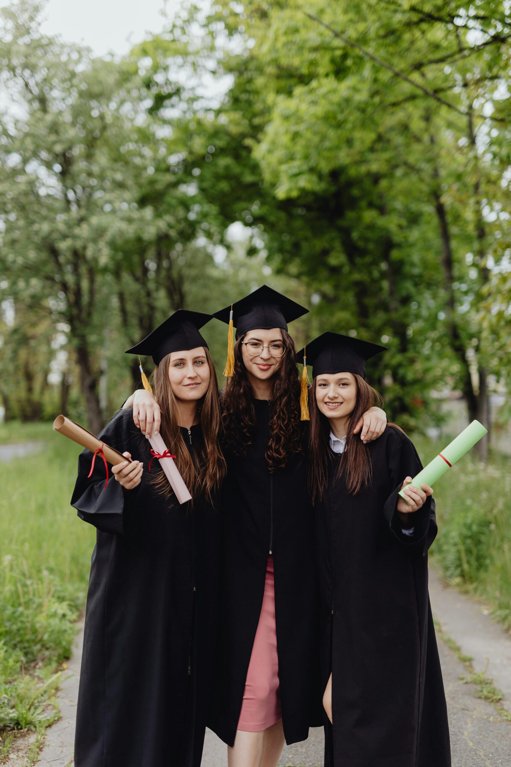 Three young women in graduation gowns celebrating together outdoors.